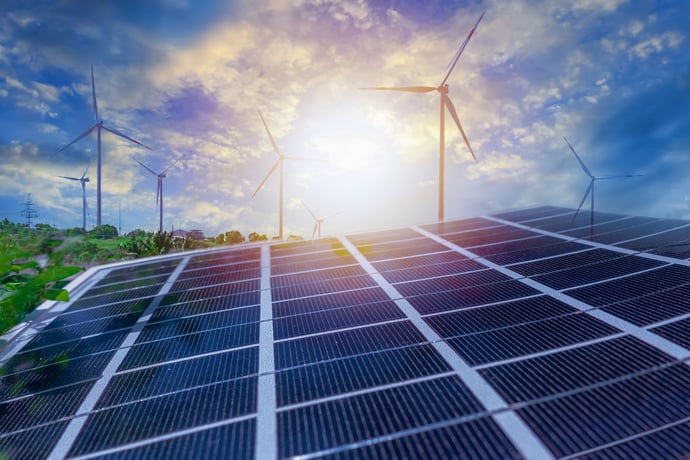 placas solares à frente, com torres eólicas ao fundo e o por de sol, ilustrando a geração de energia renovável